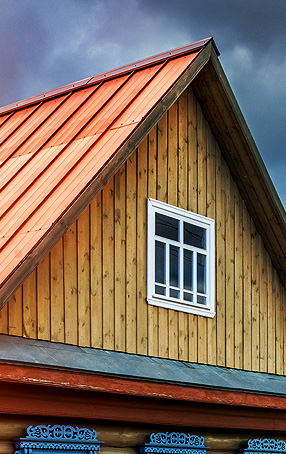 Roof with orange metal shingles and wooden siding, showcasing a white window, representing durable roofing solutions for Arizona homes.