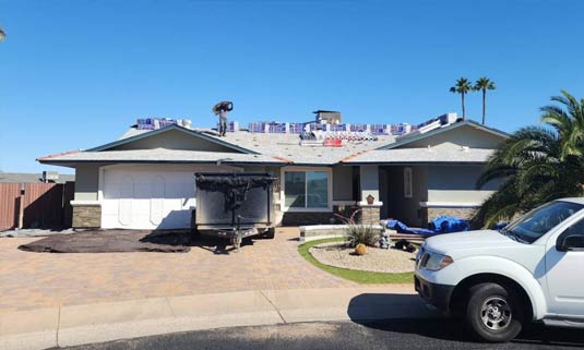 Residential home undergoing roofing installation, featuring new materials on the roof, construction equipment in the driveway, and a clear blue sky, emphasizing Ironclad Roofing's commitment to quality workmanship and solar coordination.