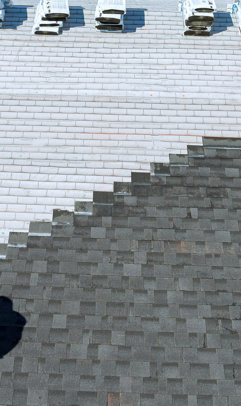 Roofing installation showcasing a transition between gray shingle tiles and lighter roofing materials, with roofing stacks visible, emphasizing Ironclad Roofing's craftsmanship and expertise in roofing solutions.