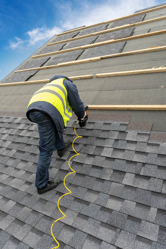 Roofing contractor installing asphalt shingles on a sloped roof, using a nail gun, with safety vest and tools, emphasizing durable roofing solutions for Arizona's climate.