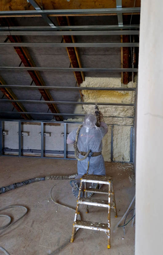 Attic spray foam insulation installation by a professional wearing protective gear, demonstrating energy-efficient insulation application in a residential setting.