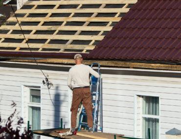 Worker on ladder installing new metal roofing on residential home, emphasizing quality roofing services for Cave Creek homes.