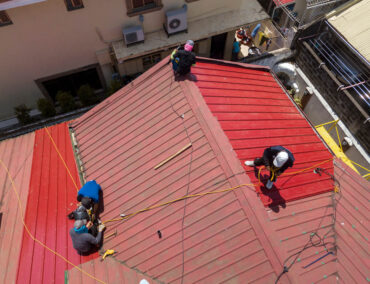 Roofers installing a red metal roof, showcasing teamwork and expertise in roofing services, relevant to Ironclad Roofing's offerings in Cave Creek, AZ.