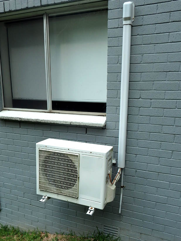 DC mini-split outdoor condenser unit mounted on gray brick wall, showcasing clean line set routing and secure installation for energy-efficient cooling solutions.