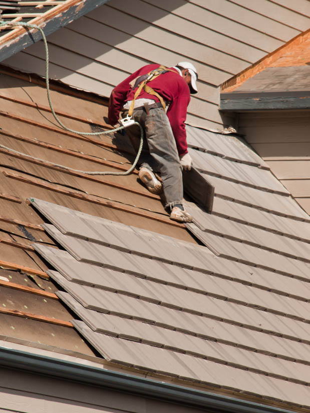 Roofer installing new shingles on a residential roof, demonstrating quality craftsmanship and safety measures during an insurance roof replacement in Arizona.