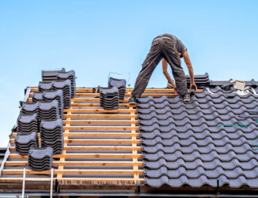 Roofing contractor installing dark tile roofing on a residential home in Mesa, showcasing craftsmanship and roofing materials relevant to local climate needs.