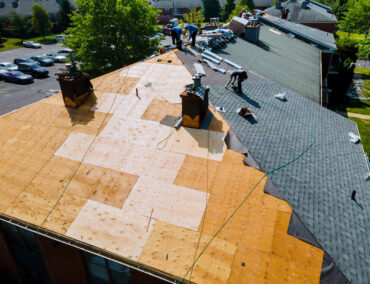 Roofing installation in progress, workers replacing shingles on a residential building in Mesa, showcasing asphalt and plywood materials.