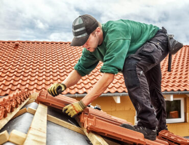 Roofer installing clay tiles on a sloped roof, showcasing craftsmanship and attention to detail in roofing services for Prescott homes.