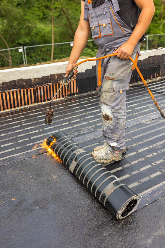 Worker installing rolled roofing material with a torch on a flat surface, demonstrating the application process for durable roofing solutions.