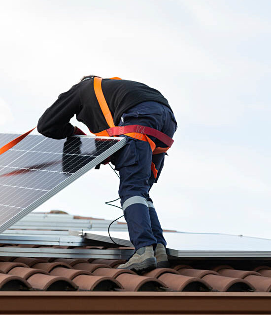 Worker in safety harness handling solar panel on a roof during solar detach and reset process, showcasing expertise in roofing and solar installation for Arizona homeowners.
