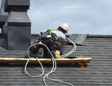 Roofer installing asphalt shingles on a residential roof in Tucson, showcasing expert craftsmanship and safety equipment, relevant to Ironclad Roofing's services.